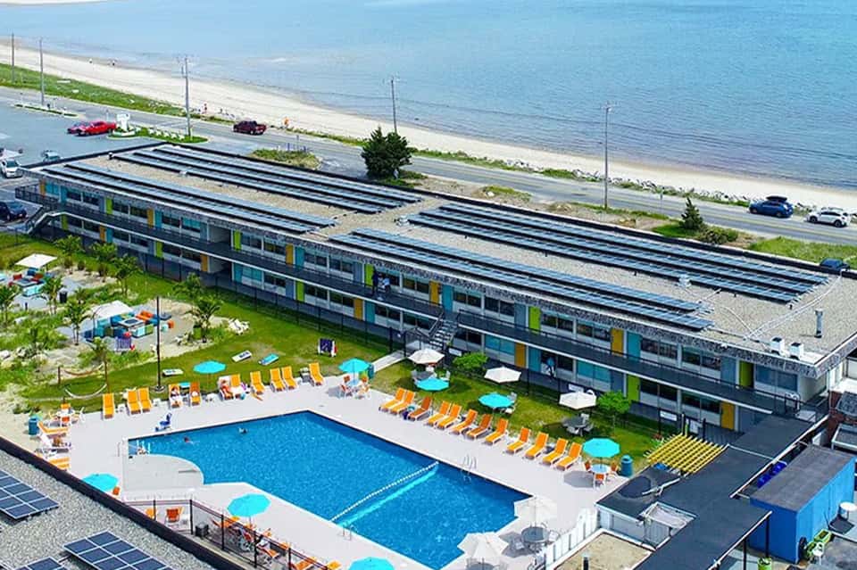 Beachfront resort with solar panel roof, swimming pool, yellow lounge chairs, and ocean view