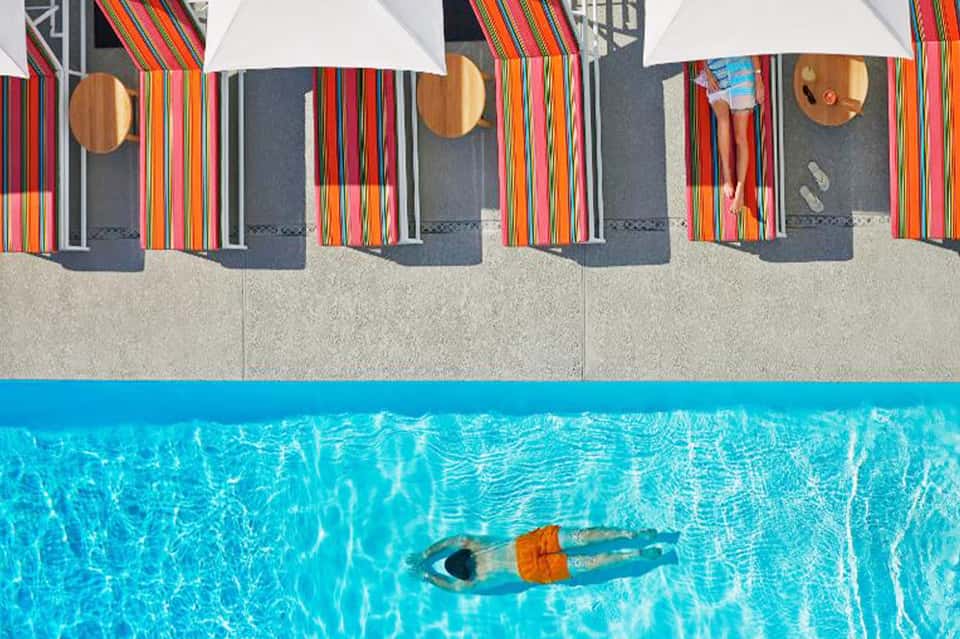 Aerial view of poolside with colorful striped beach umbrellas, lounge chairs, and swimmer
