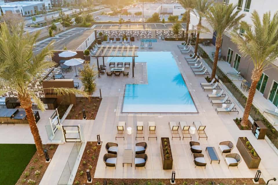 Aerial view of resort pool deck with lounge chairs, palm trees, and modern architecture