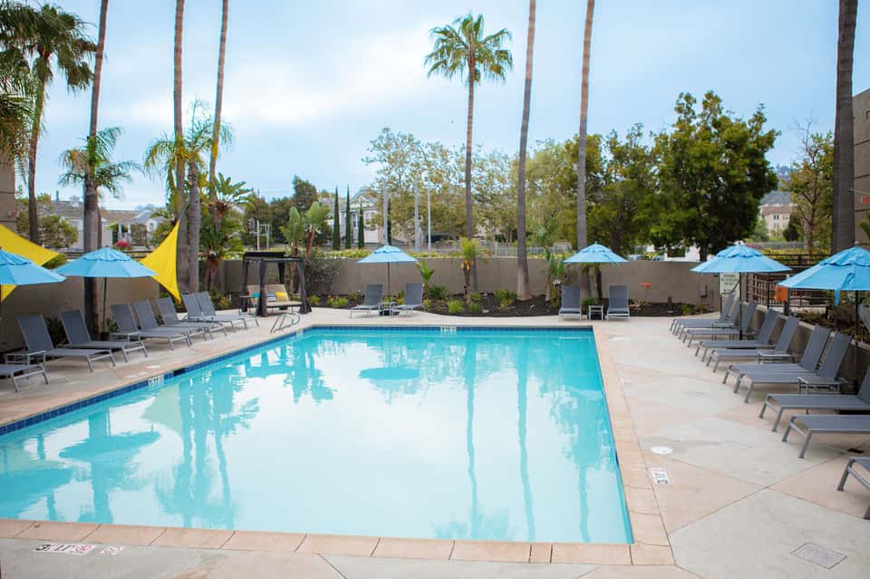 Resort swimming pool surrounded by palm trees, blue umbrellas, and lounge chairs