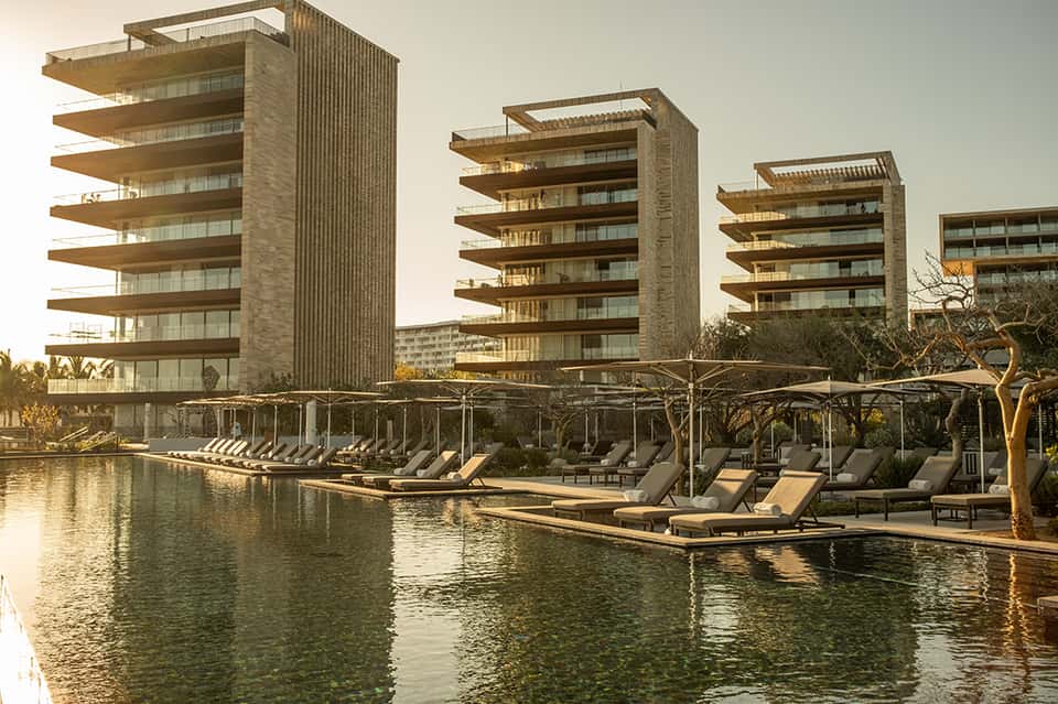 Multi-story residential towers reflected in waterfront with lounge chairs on dock and landscaping