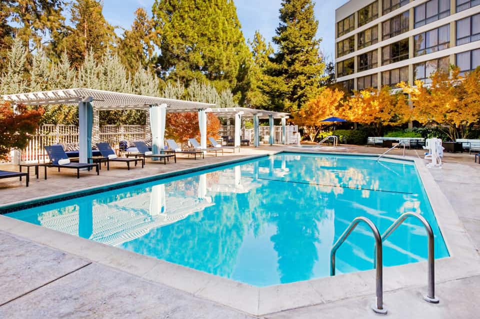 Resort pool surrounded by fall foliage with white pergola and lounge chairs