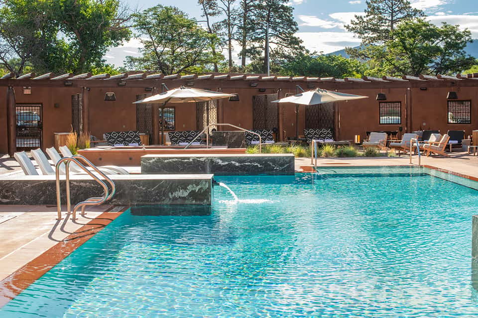 Resort pool with terracotta walls, lounge chairs, umbrellas, and mountain views
