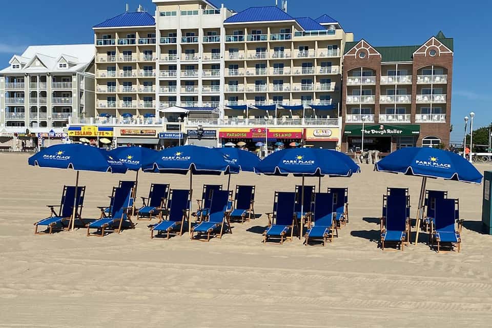 Sandy beach with blue umbrellas and lounge chairs in front of multi-story beachfront hotel