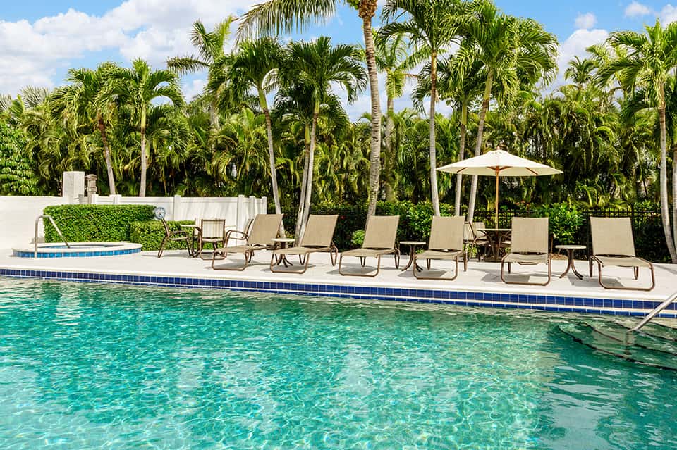 Resort pool with crystal-clear turquoise water, lounge chairs, palm trees, and white umbrellas