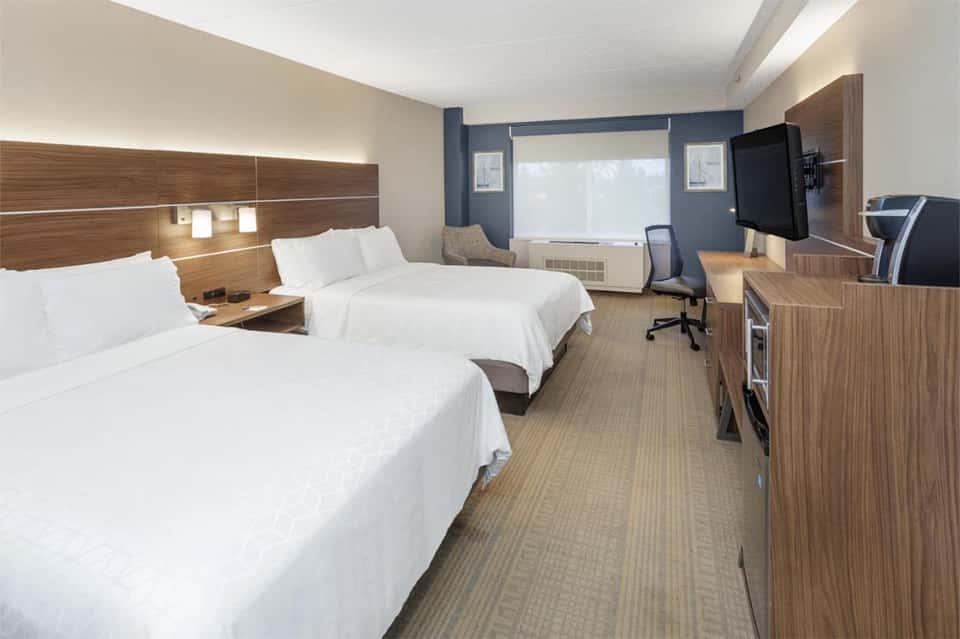 Modern hotel room with two queen beds, wood headboards, blue accent wall, and work desk