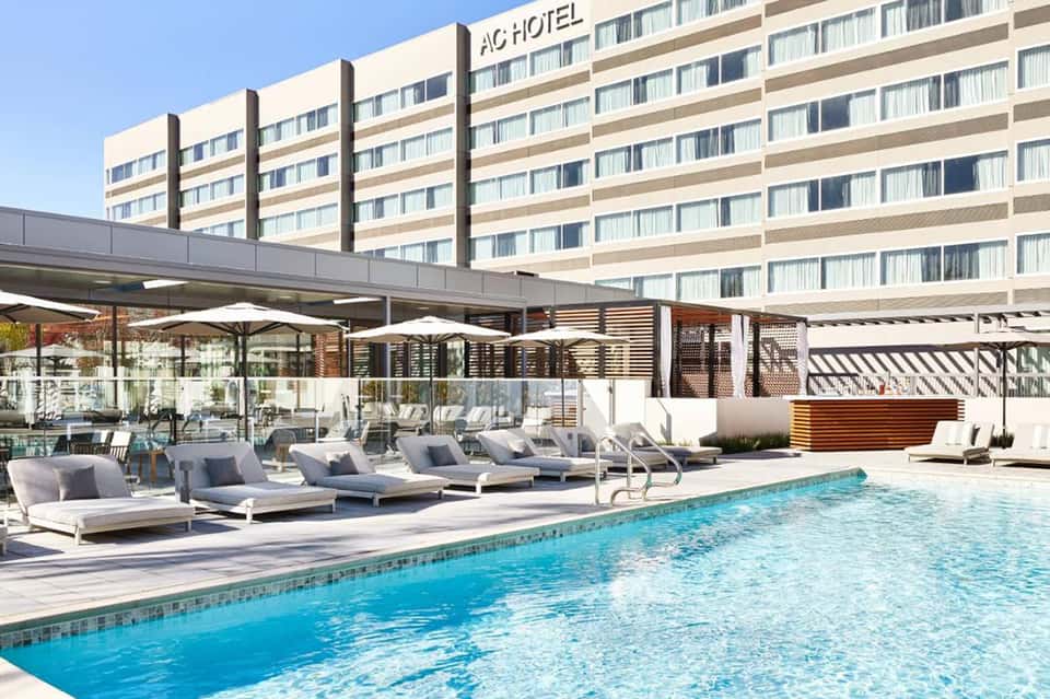 Hotel pool with blue water, white lounge chairs, beige umbrellas, and beachfront building