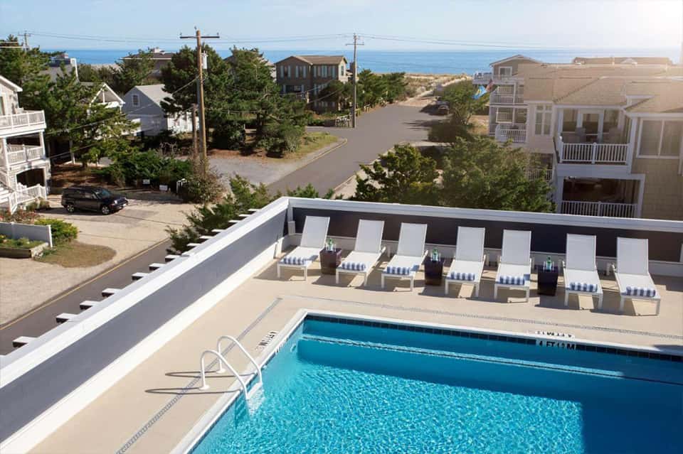 Rooftop pool deck with white lounge chairs, ocean views, and residential buildings in coastal setting