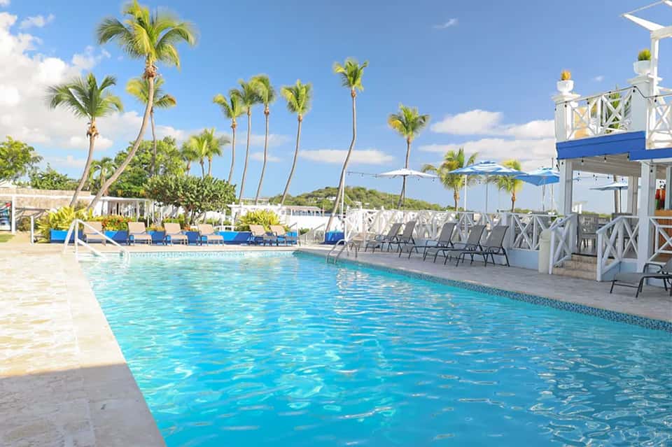 Resort swimming pool with blue water, palm trees, white lounge chairs, and cabana area