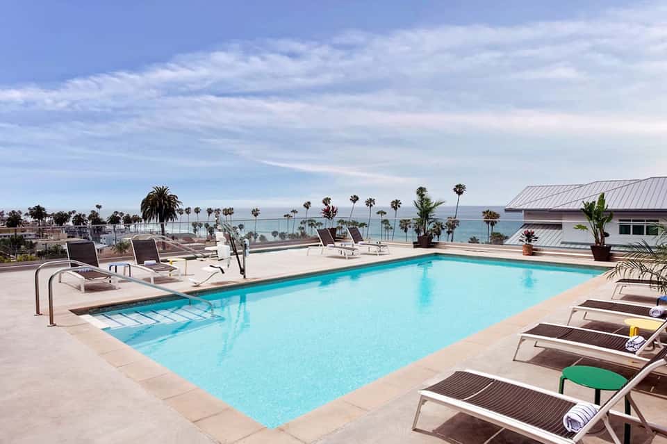 Oceanfront swimming pool with lounge chairs, palm trees, and coastal views