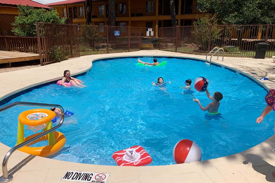 Children swimming in a bright blue pool with inflatable toys and water games