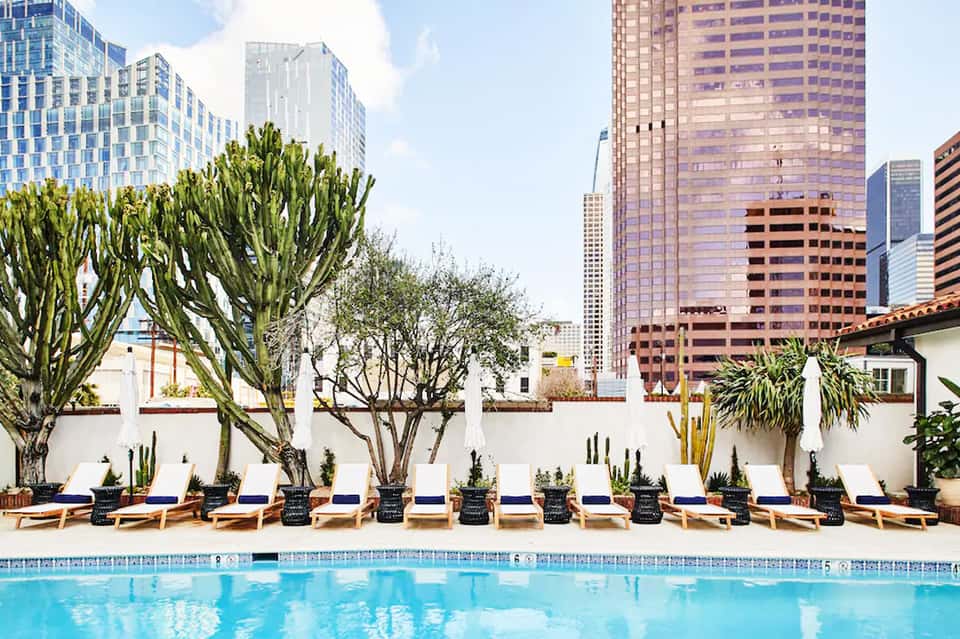 Modern hotel pool with lounge chairs, cacti, and white walls overlooking downtown city skyline