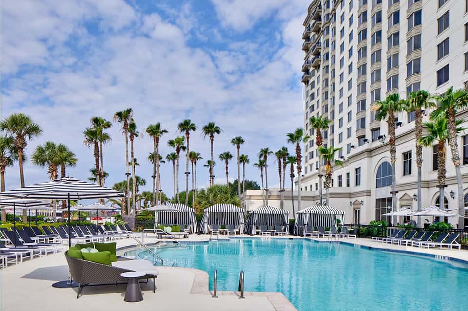 Luxury resort pool with palm trees, loungers, umbrellas, and high-rise building with classical architecture