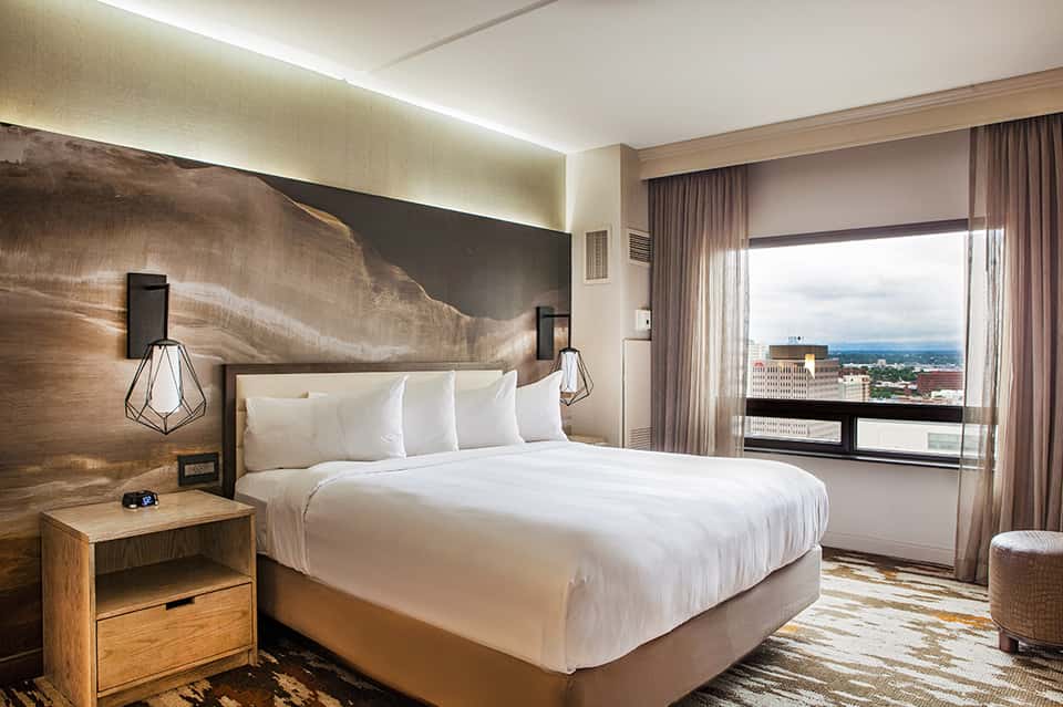 Contemporary hotel bedroom with king bed, wood accent wall, and city skyline view