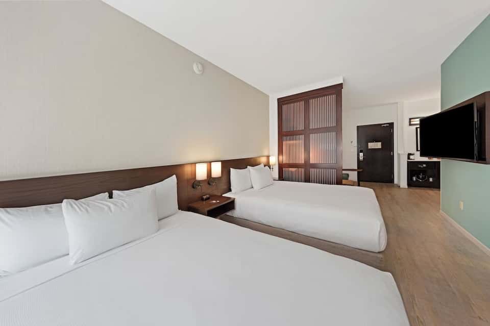 Contemporary hotel room with two queen beds, dark wood headboard, and mint accent wall