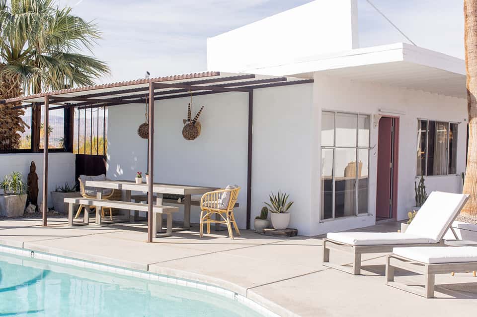 Modern white resort building with covered patio, dining area, and pool deck with palm trees