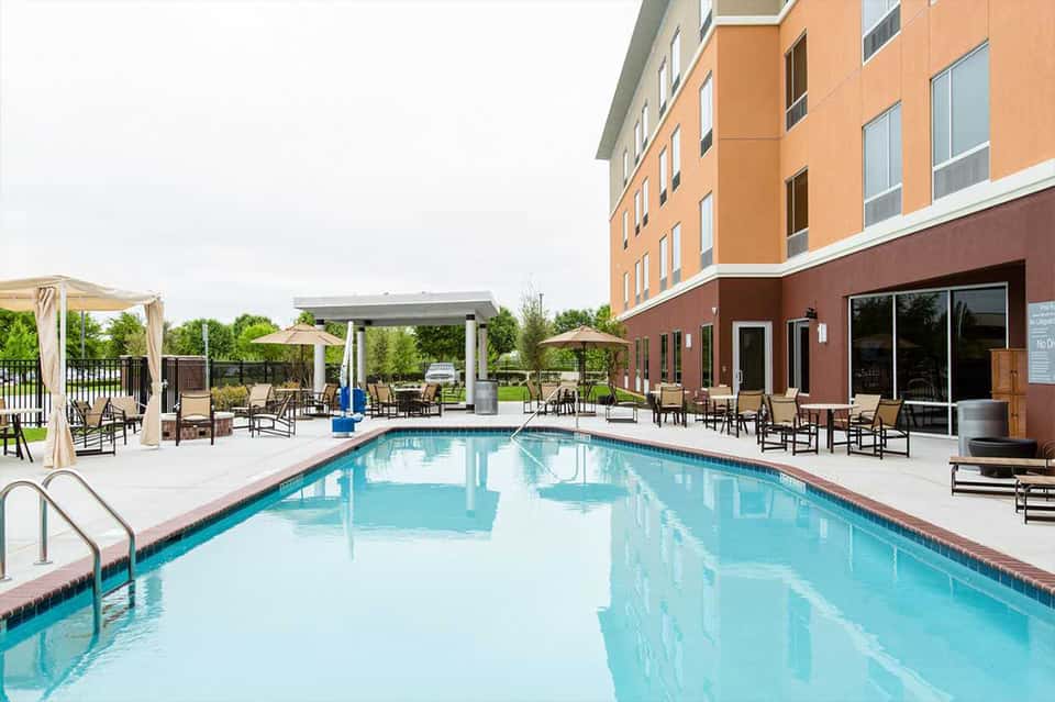 Resort outdoor pool with lounge chairs, pergola shade structures, and brick hotel building