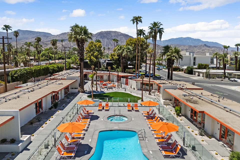 Resort pool deck with blue swimming pool, orange lounge chairs, umbrellas, and desert mountain views