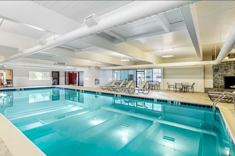 Indoor swimming pool with high ceilings, lounge chairs, and stone fireplace
