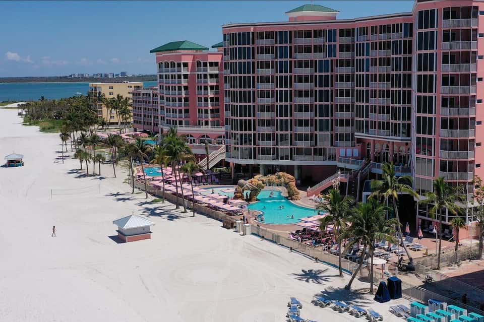Aerial view of pink beachfront resort with multiple pools, white sand beach, and palm trees