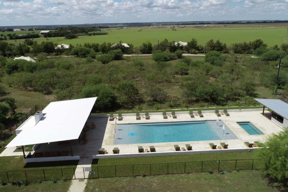 Aerial view of resort pool complex with white shade structure and lounge chairs overlooking rural landscape