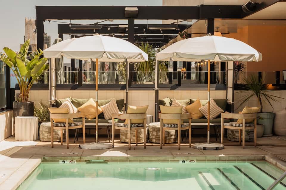 Rooftop lounge area with white umbrellas, seating, and infinity pool