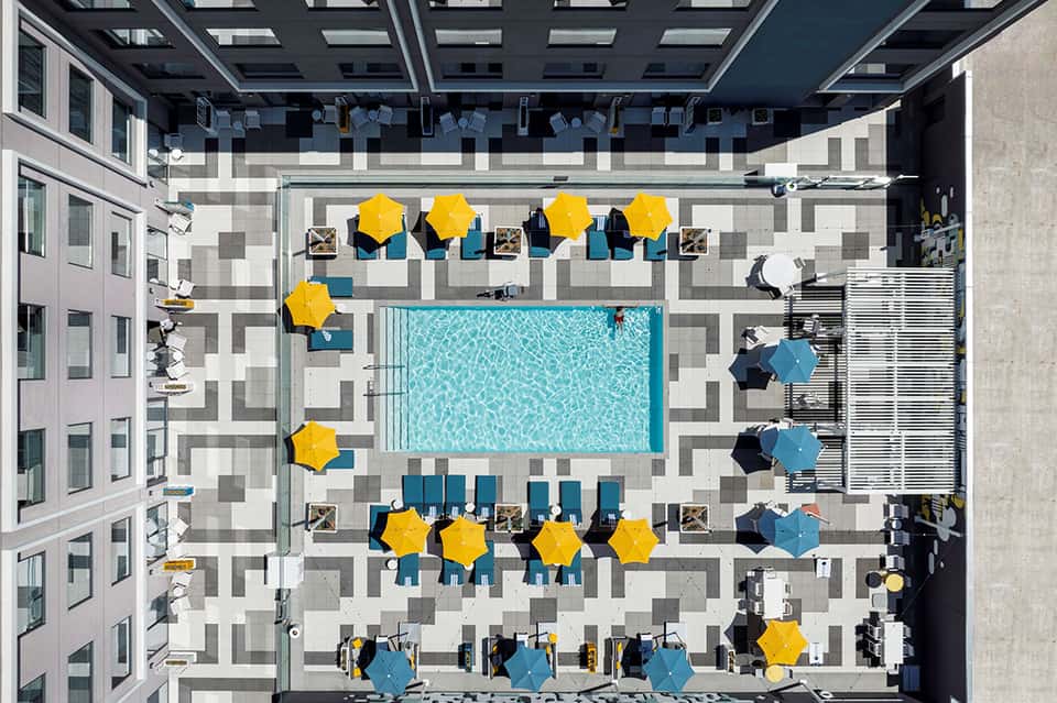 Aerial view of courtyard pool surrounded by yellow umbrellas and lounge seating