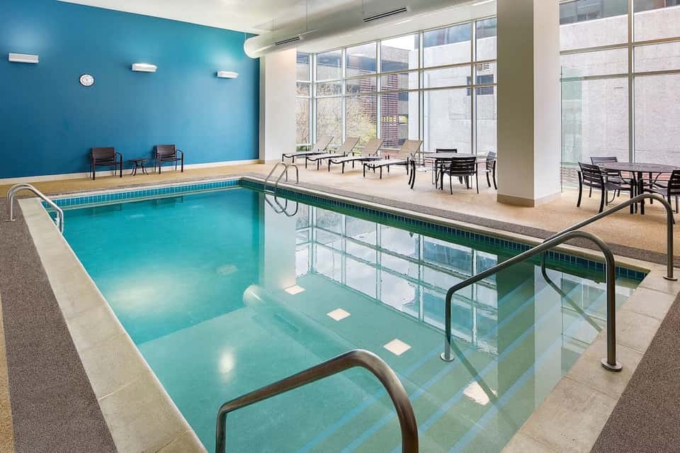 Indoor swimming pool with bright turquoise water, windows, and lounge seating area
