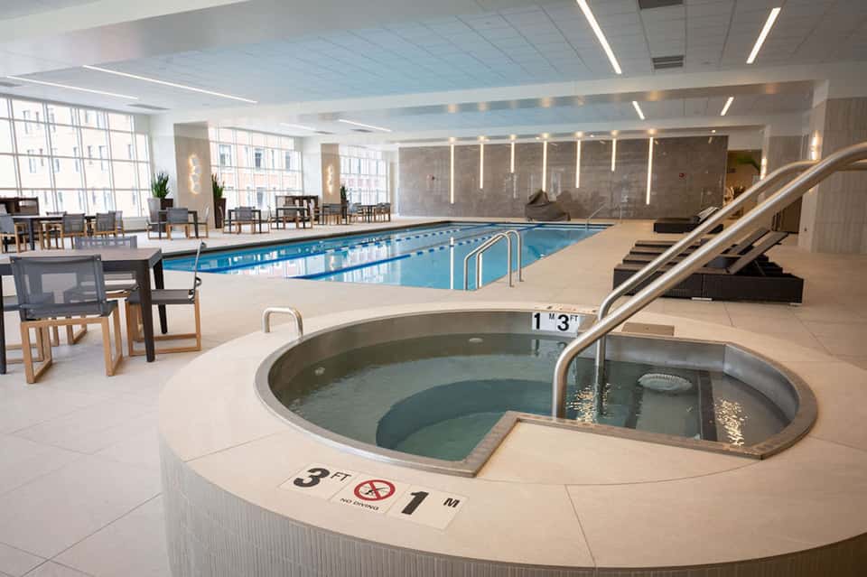 Indoor pool and hot tub facility with lap pool, spa tub, lounge chairs, and bright lighting