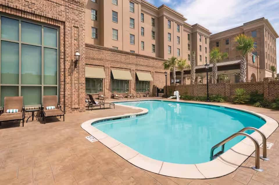 Hotel outdoor pool with lounge chairs and brick building facade with palm trees