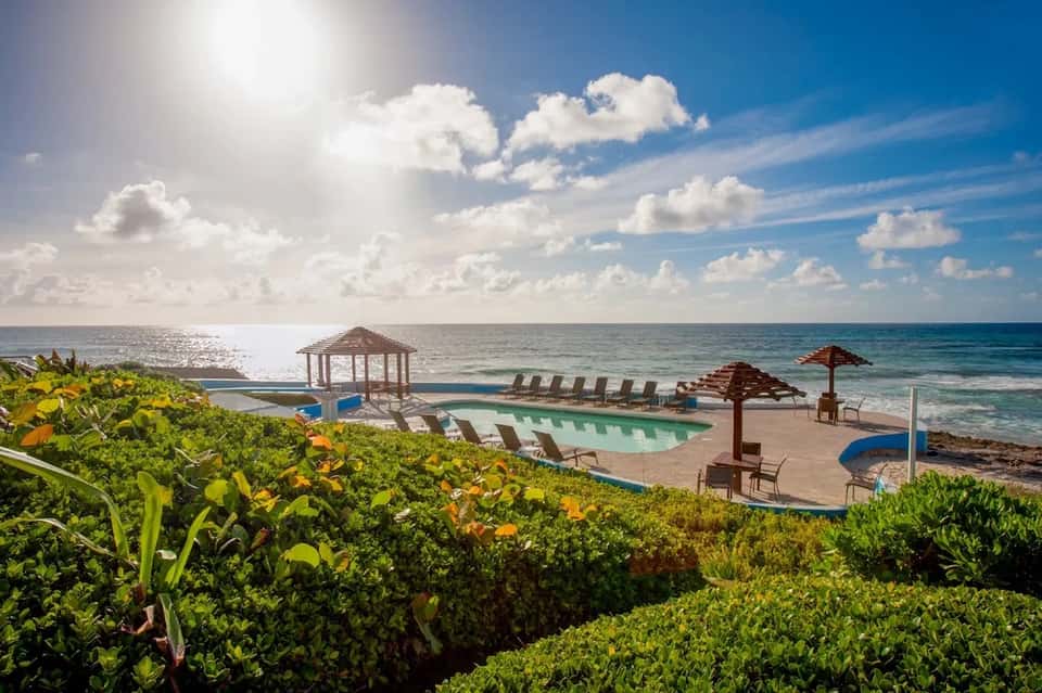 Beachfront resort pool with lounge chairs, umbrellas, and ocean view on sunny day