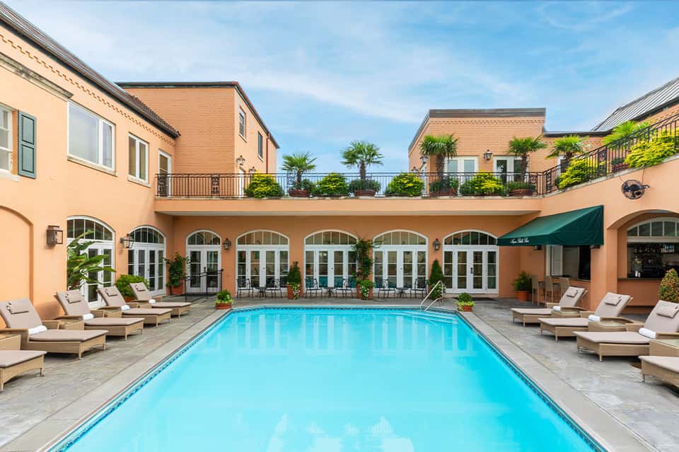 Indoor rectangular pool with cream loungers, arched columns, and terracotta building facade reflected in calm water