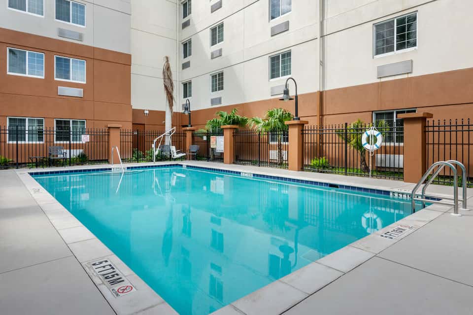 Indoor hotel swimming pool surrounded by brown walls, black fence, and manicured landscaping