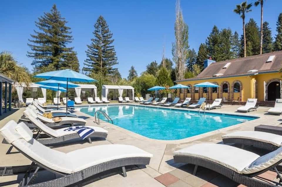 Resort pool with blue umbrellas, lounge chairs, and yellow building facade