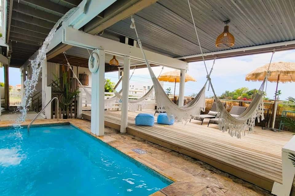 Covered pool deck with white hammocks, hanging seating areas, and tropical beach setting
