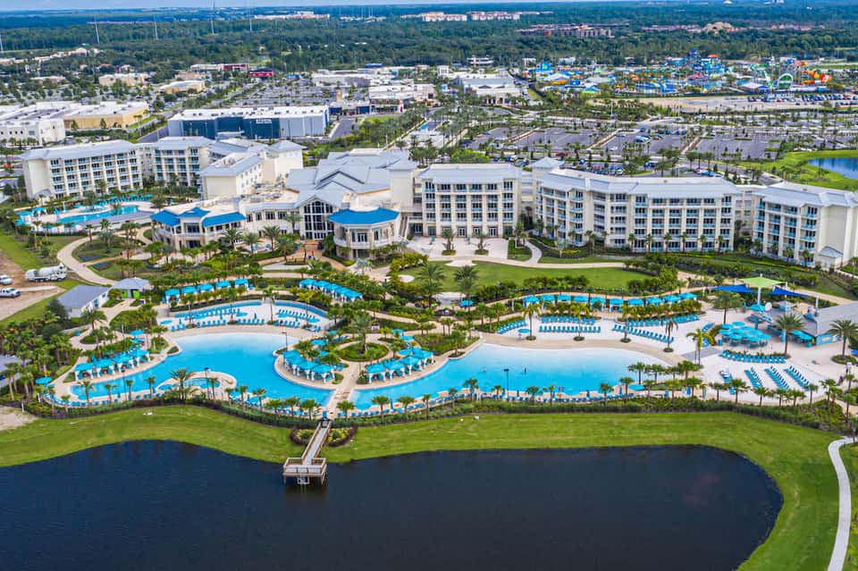 Aerial view of resort with multiple blue-water pools, white buildings, palm trees, and tropical landscaping