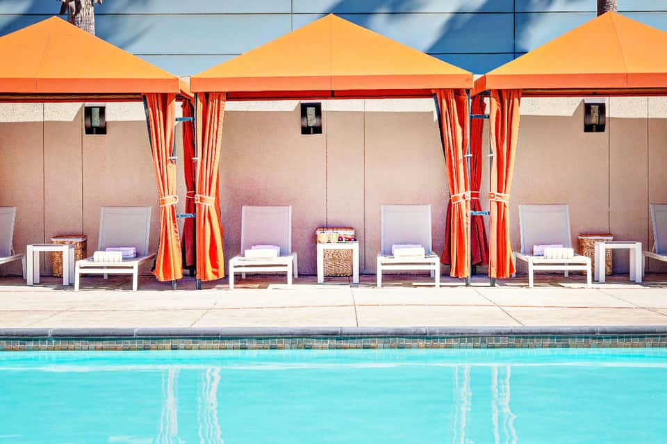 Poolside cabanas with orange umbrellas and white loungers beside turquoise swimming pool