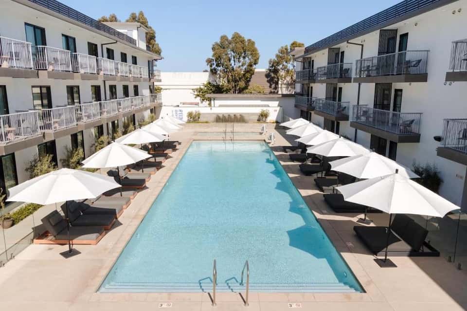 Luxury hotel courtyard with rectangular pool, white umbrellas, black loungers, and surrounding apartments