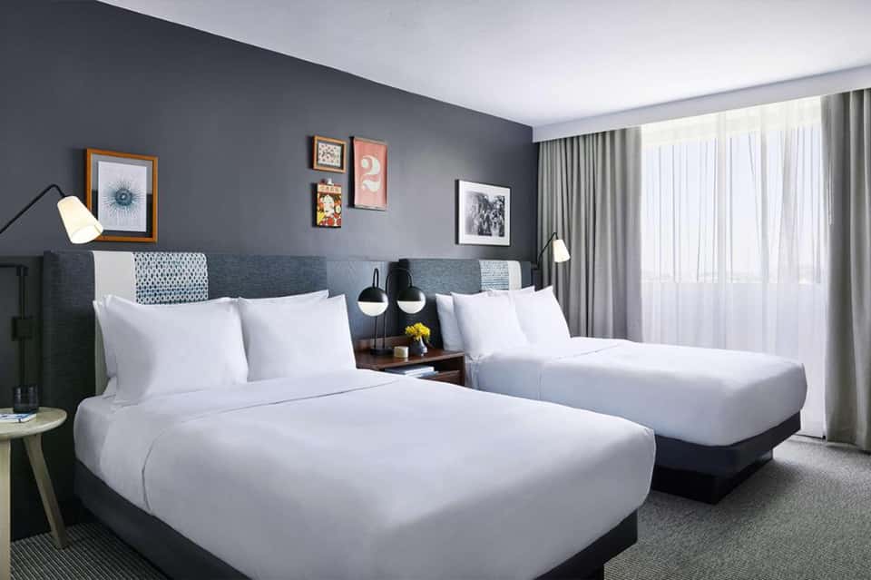 Hotel guest room with two queen beds, gray headboard, modern lighting, and ocean view windows