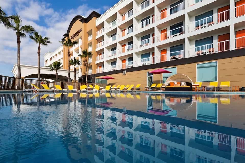 Resort pool with yellow lounge chairs and multi-story building with colorful balconies