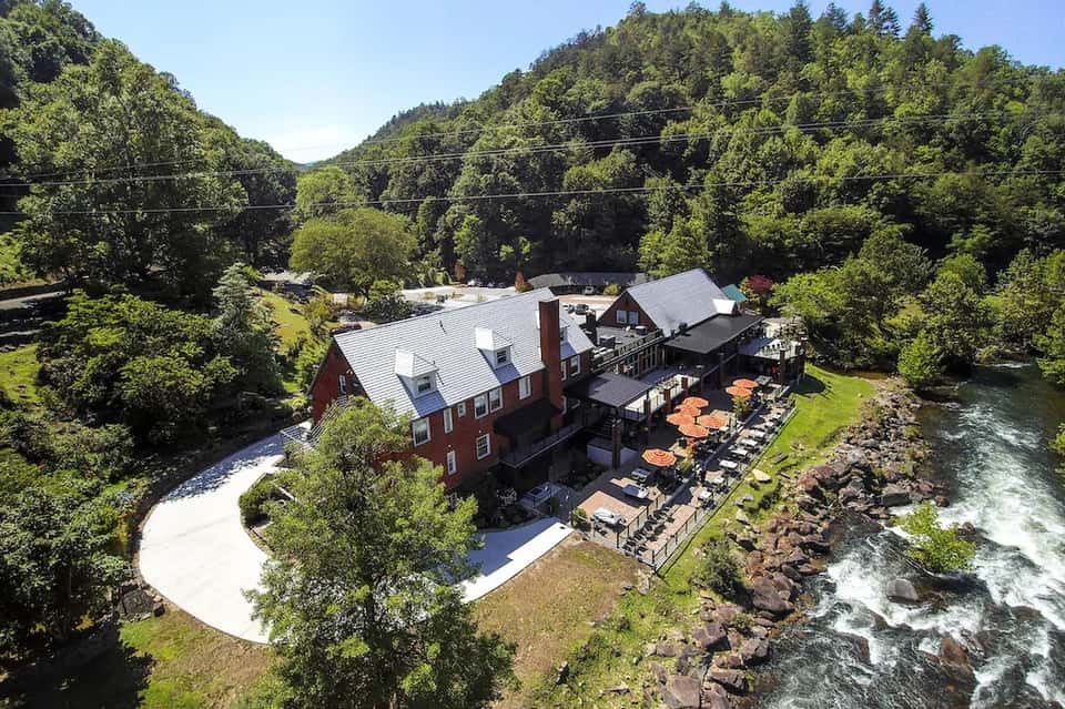 Red brick riverside resort nestled in forested mountains with outdoor seating and flowing river views