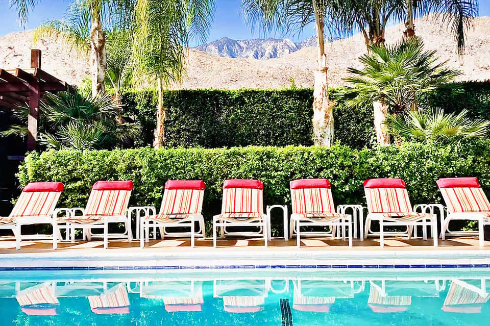 Red and white striped lounge chairs lined up by pool with palm trees and desert mountains