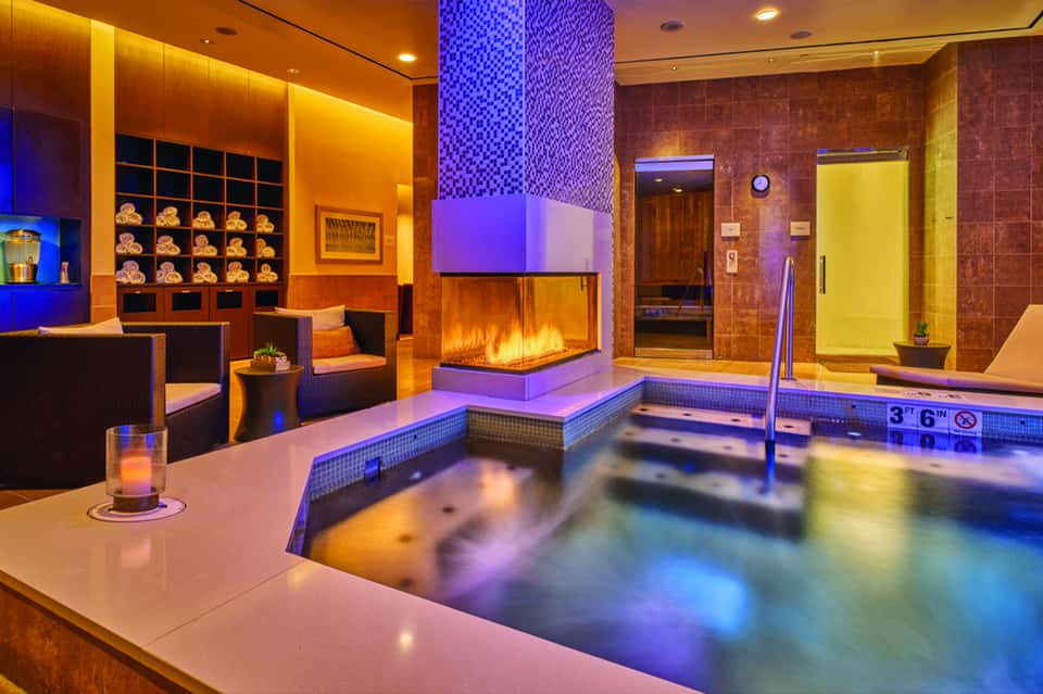 Luxury spa area with indoor pool, fireplace, mosaic tile work, and warm amber lighting