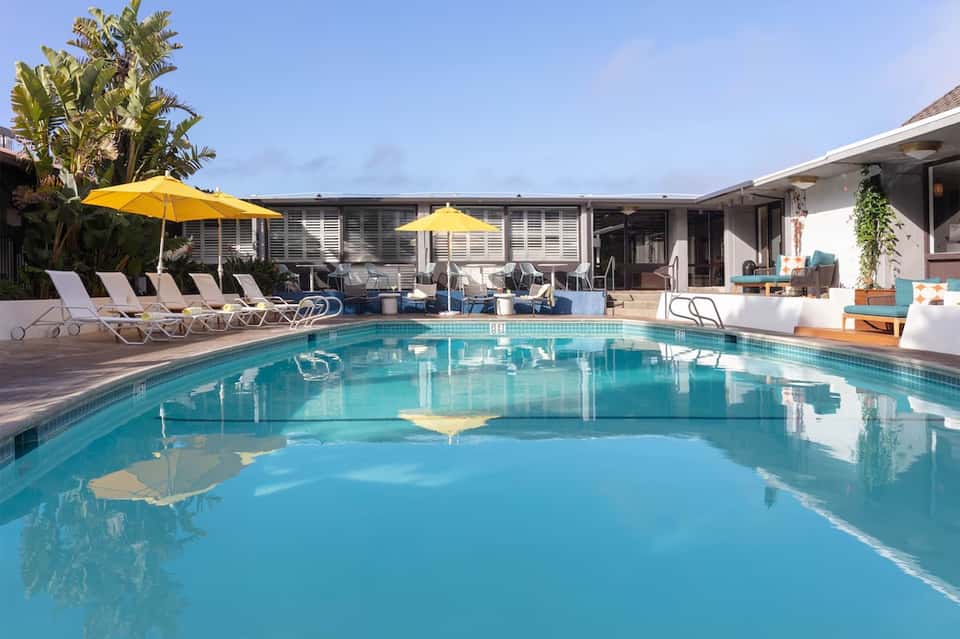 Luxury pool area with turquoise water, yellow umbrellas, lounge chairs, white building, and palm landscaping