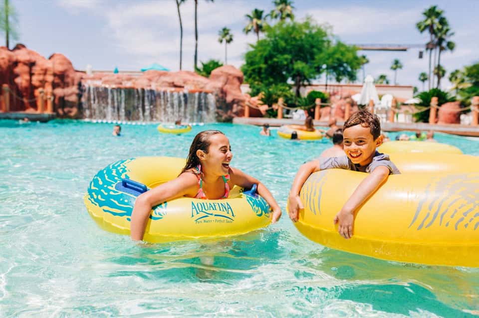 Children enjoying yellow inflatable tubes in bright turquoise resort pool water