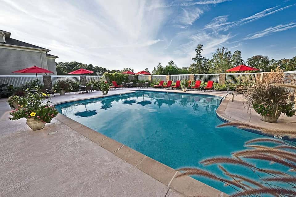 Residential pool with red umbrellas, white fence, lounge chairs, and manicured lawn area