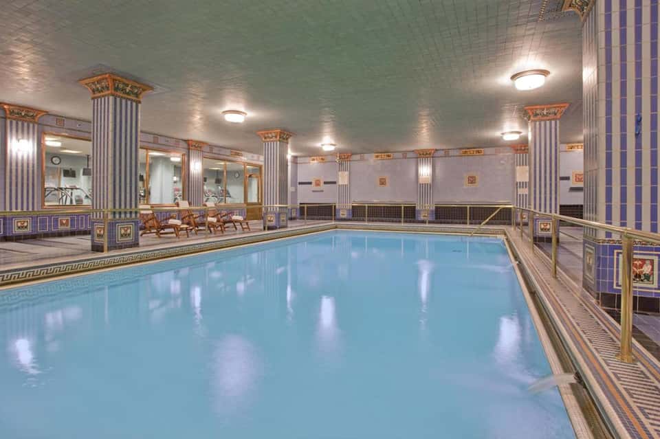 Elegant indoor swimming pool with decorative columns, ornate details, and pristine blue water