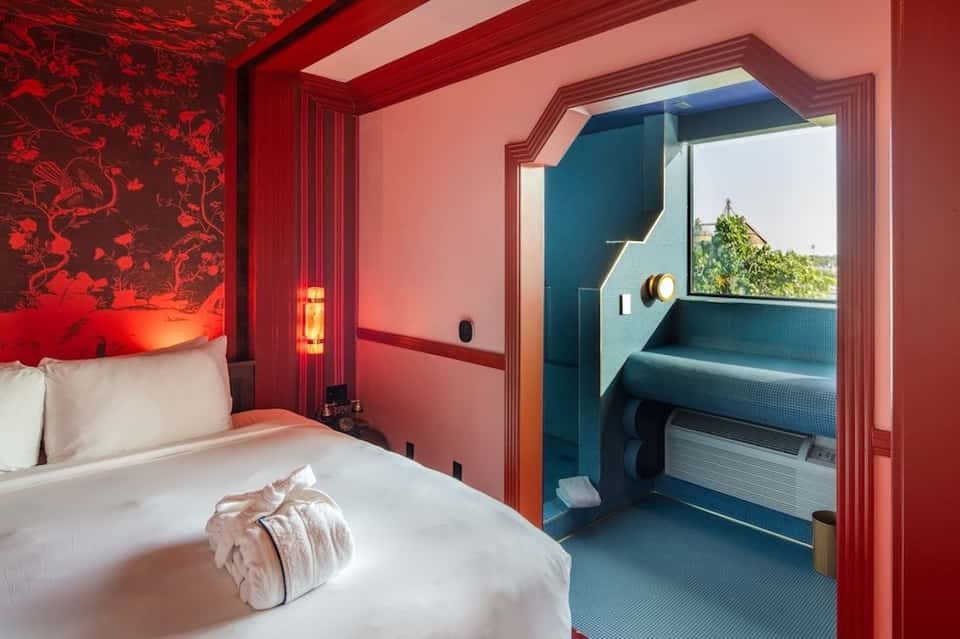 Boutique hotel bedroom in red with connecting spa room featuring soaking tub