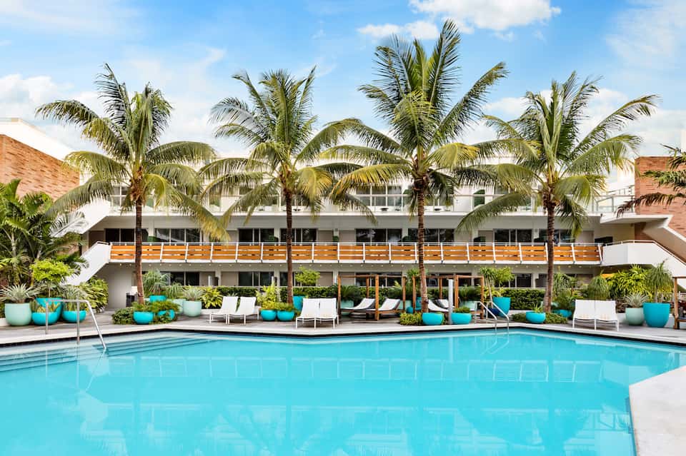 Resort pool with turquoise water, palm trees, white lounge chairs, and modern building facade with wooden accents