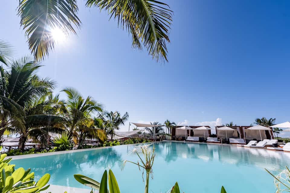 Tropical resort pool surrounded by palm trees, lounge chairs, and white cabanas